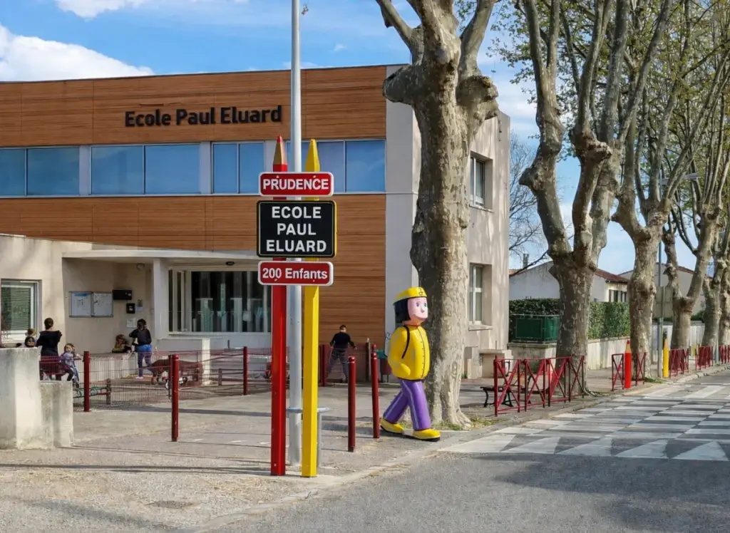 Entrée principale d'école sécurisée par un totem crayon et une figurine de signalisation